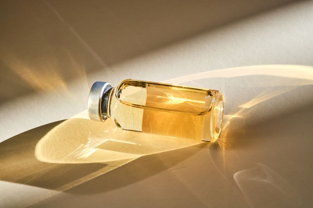 Small glass perfume bottle with amber liquid, lying on a sunlit surface
