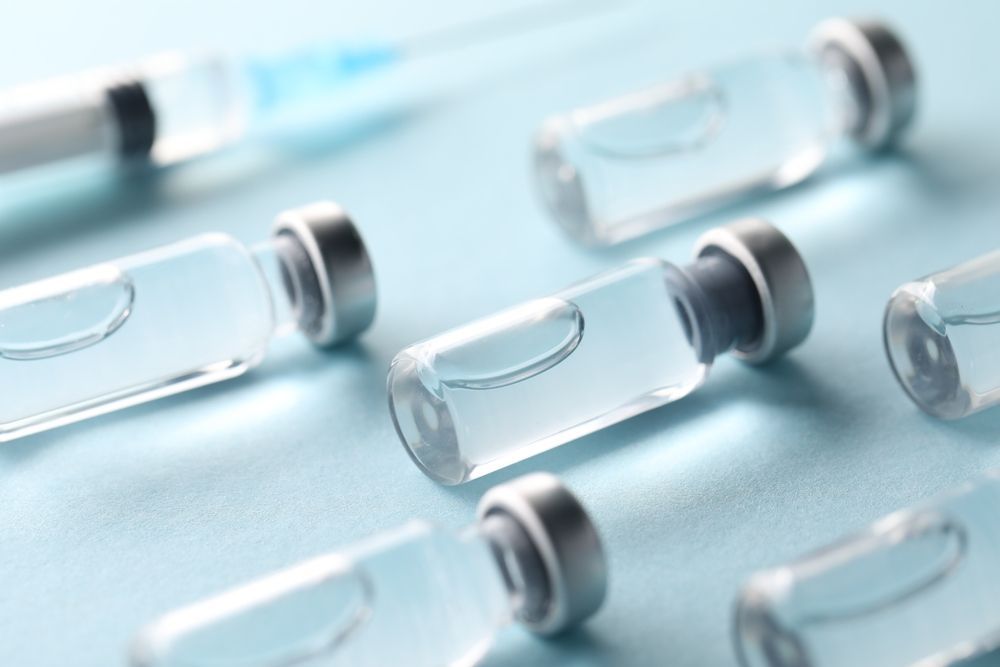 Glass vaccine vials with gray caps on a light blue surface