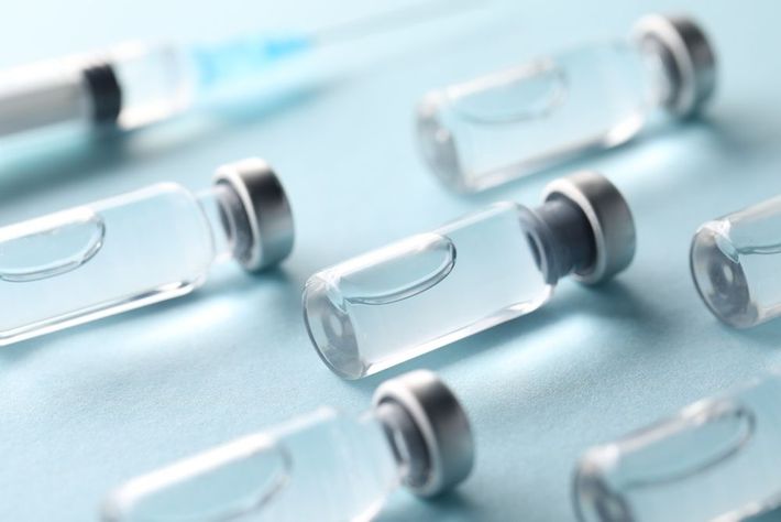Glass vaccine vials with gray caps on a light blue surface