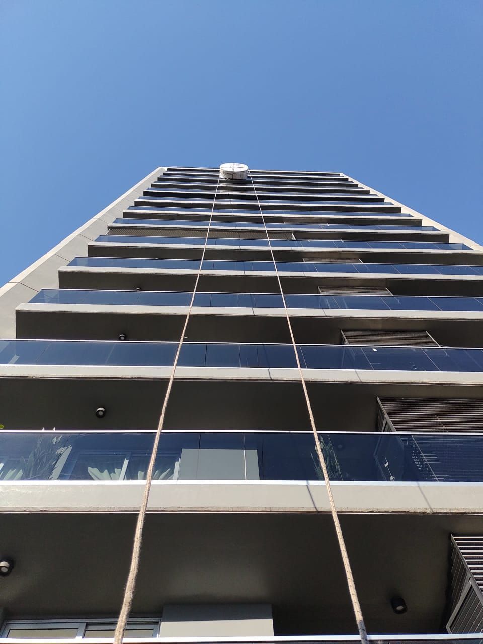 Vista desde abajo de un edificio alto y moderno contra un cielo azul claro. El edificio tiene balcones de cristal.