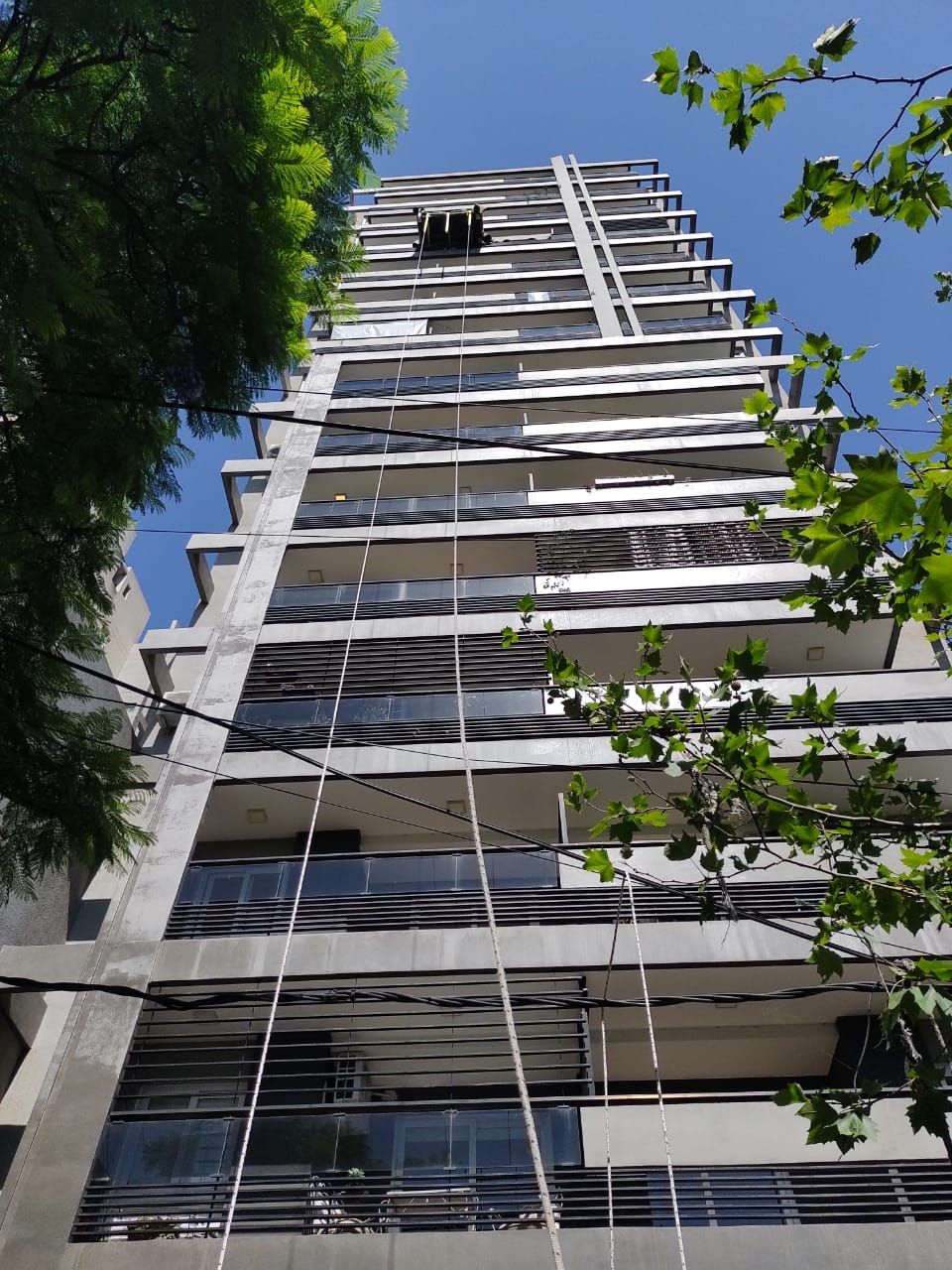 Edificio de apartamentos alto y moderno con balcones, visto desde abajo, contra un cielo azul.