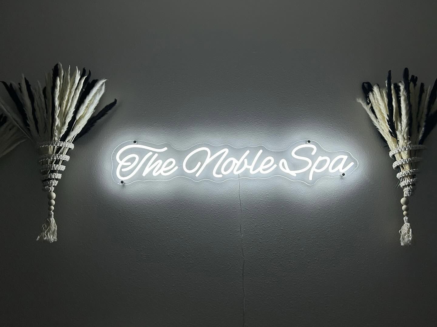 A neon sign for the noble spa is hanging on a wall.
