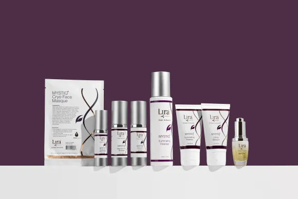 A variety of cosmetics are lined up on a table against a purple background.