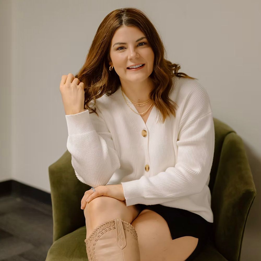 A woman is sitting in a chair wearing a white sweater and boots.