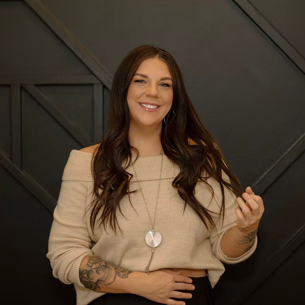 A woman with a tattoo on her arm is smiling and holding her hair.