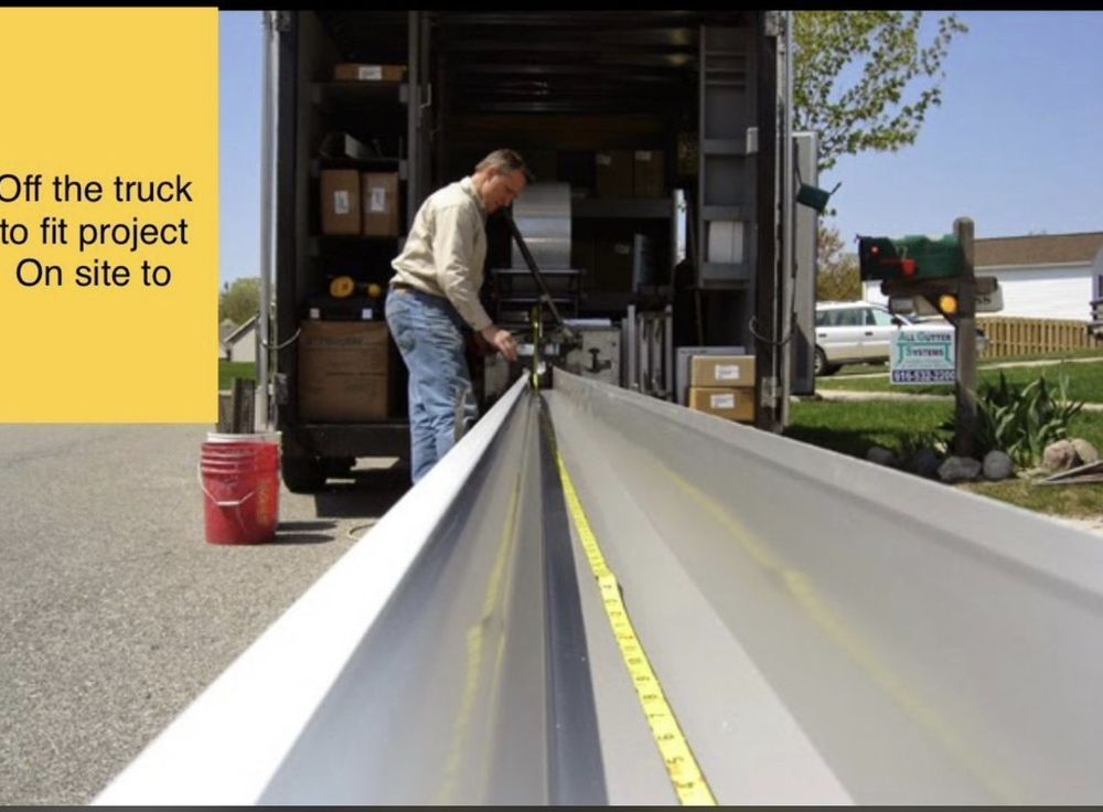 Man measures metal gutter with tape, outside a truck, on a residential site.