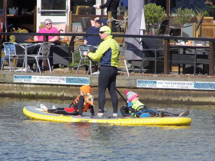 man on paddle board with two small children on calm water on River Bure, Norfolk Broads.