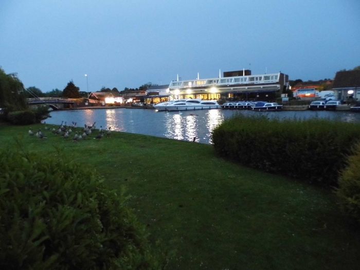 Evening view from cottage across river Bure with lights reflecting off water.