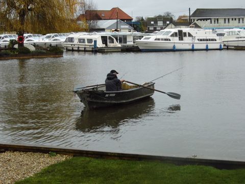 Single fisherman in fishing rowing boat on River Bure, Broads.