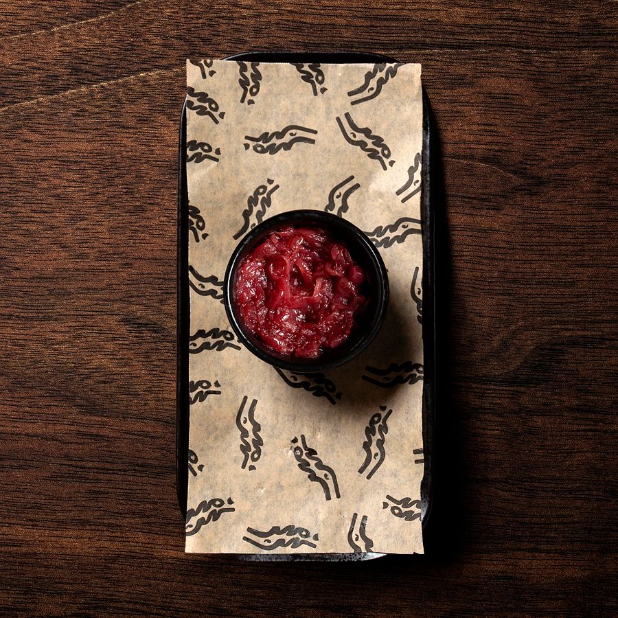 Small bowl of red sauce on patterned paper inside a black tray on a wooden surface.