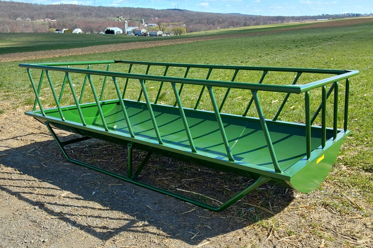 Stoltzfus Manufacturing green double-wide livestock feeder with a heavy-duty steel frame, open feeding basket, and skid-mounted base, designed for feeding cattle and other livestock.