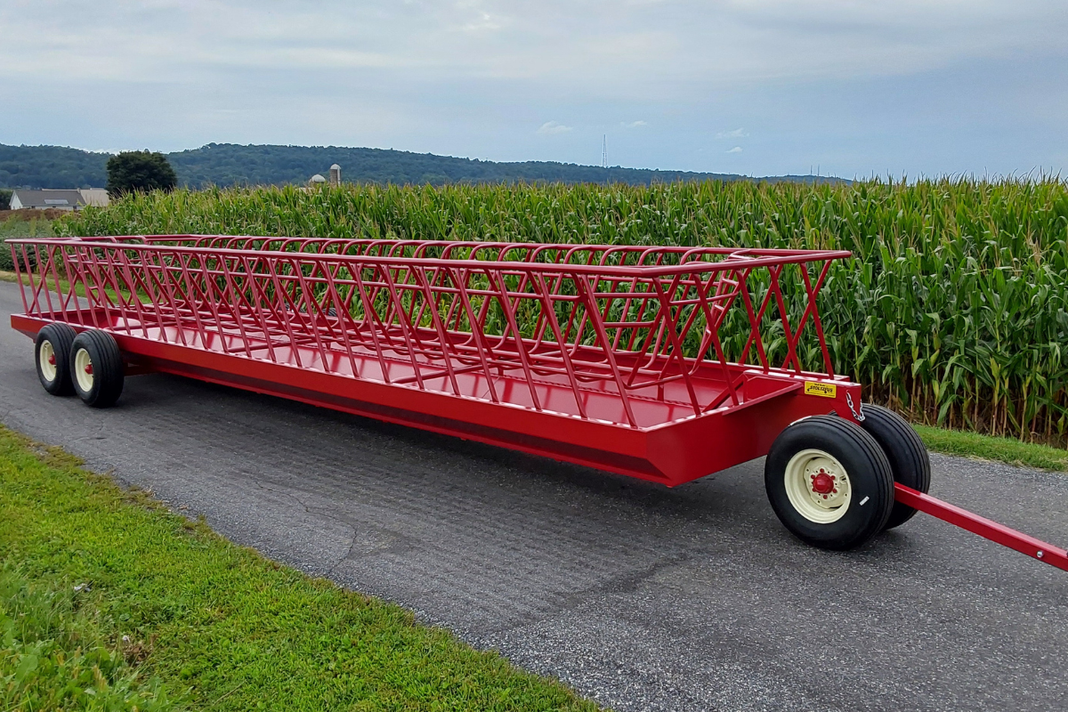 Stoltzfus Manufacturing red double-wide livestock feeder wagon featuring a long steel feeding basket, tandem rear wheels, and front towing hitch. Cow Feeder wagon
