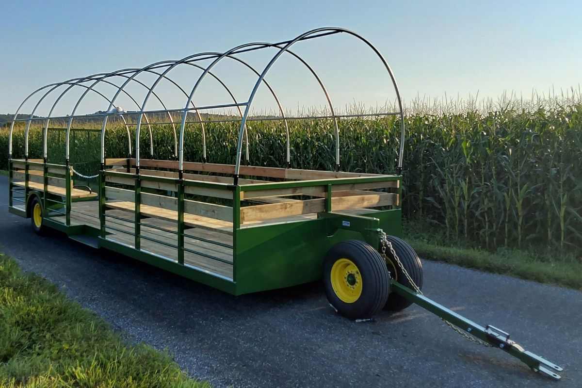 Low-profile green hayride wagon with rounded canopy frame and perimeter bench seating Stoltzfus Manufacturing