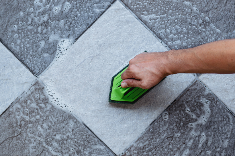 A person is cleaning a tile floor with a green sponge.