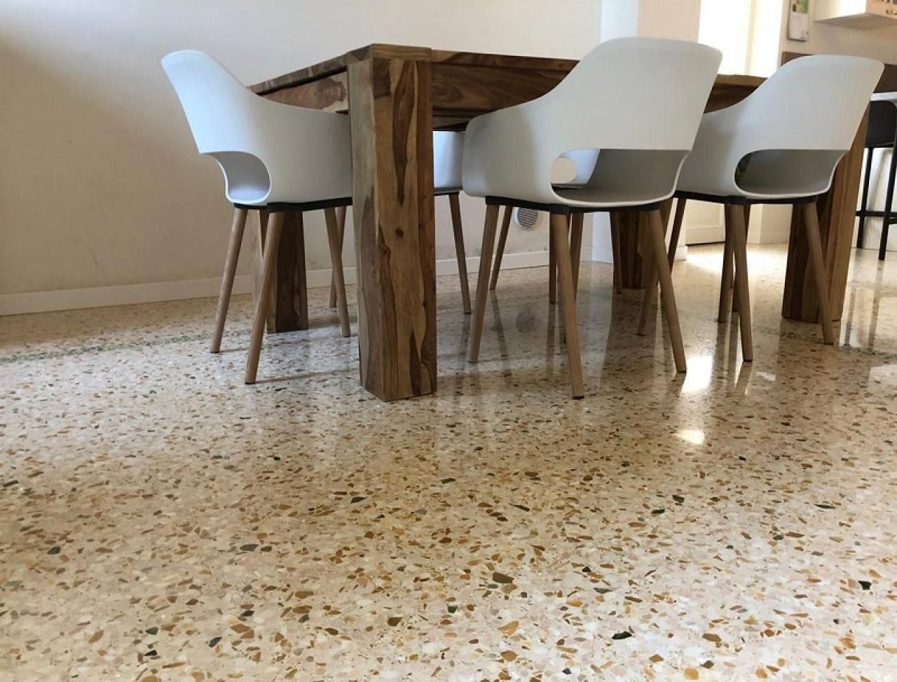 Sedie da pranzo moderne, bianche, con gambe in legno, sono disposte attorno a un tavolo in legno su un pavimento in terrazzo lucidato.