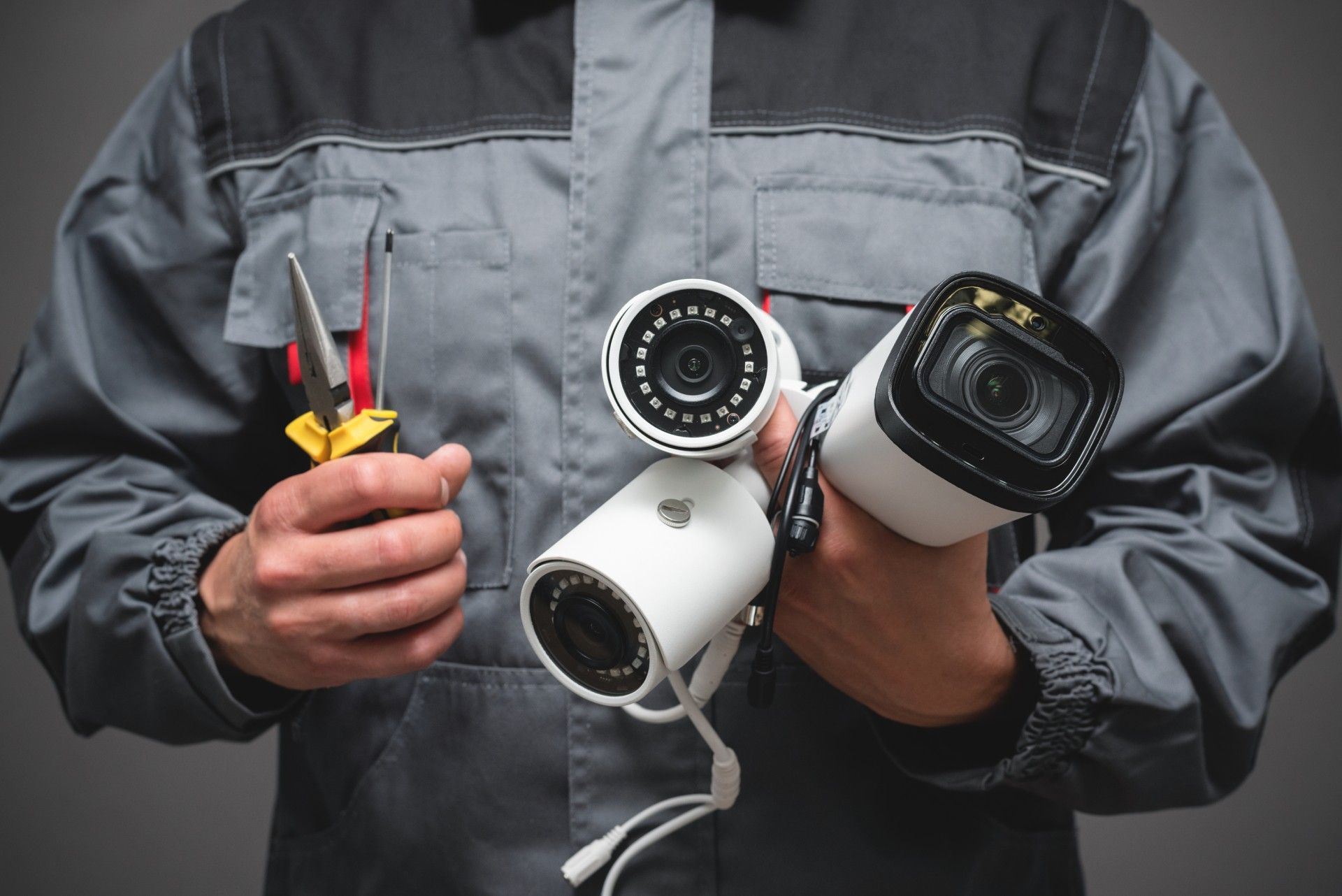 A man is holding two security cameras and a pair of pliers.