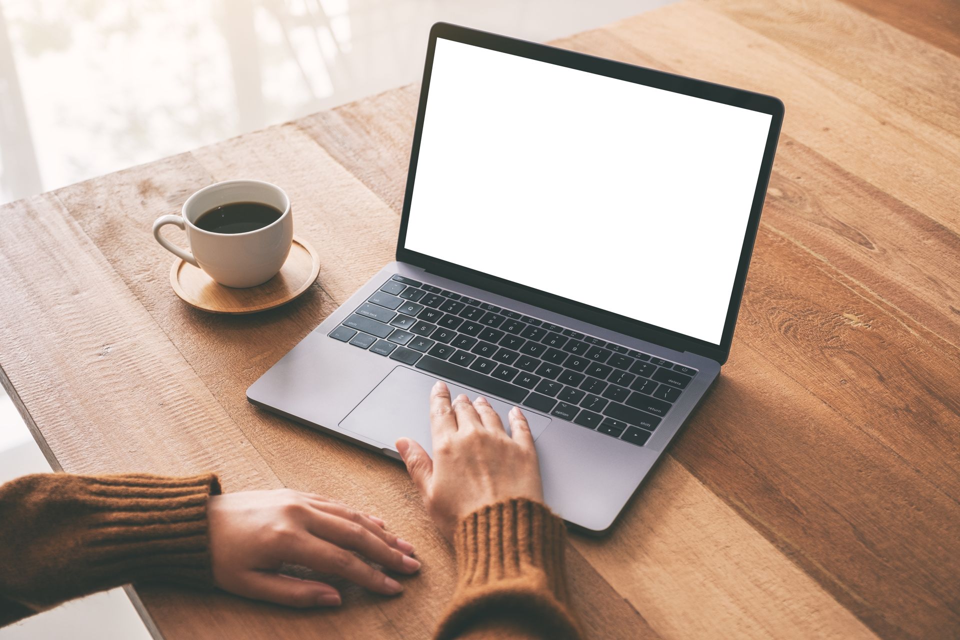 Hands typing on a laptop at a wooden table beside a cup of coffee
