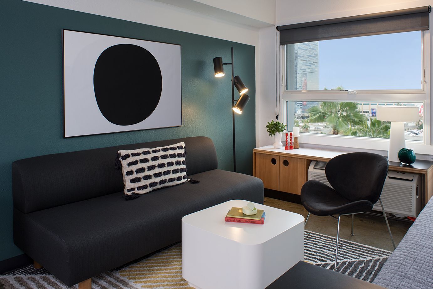 Modern living room with dark sofa, white coffee table, desk by window, and abstract wall art