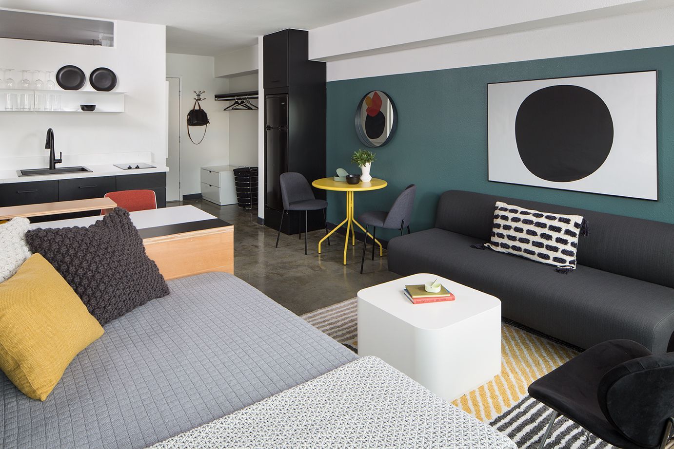 Modern living room with gray sofa, bed, yellow accents, and teal walls