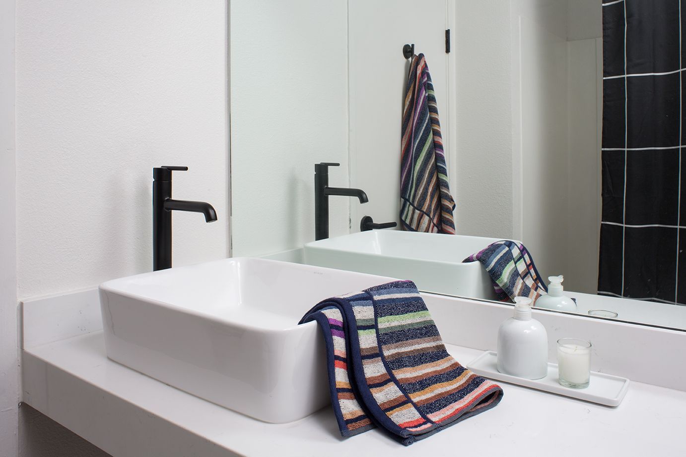 Modern bathroom vanity with rectangular sink, black faucets, mirror, and striped towels on the counter