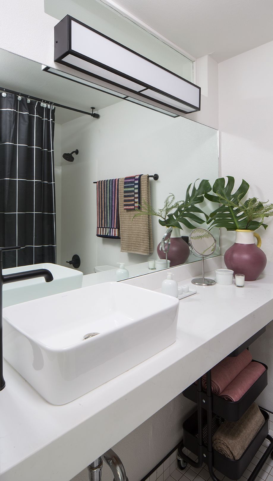 Modern bathroom vanity with white sink, mirror, plants, and dark curtains