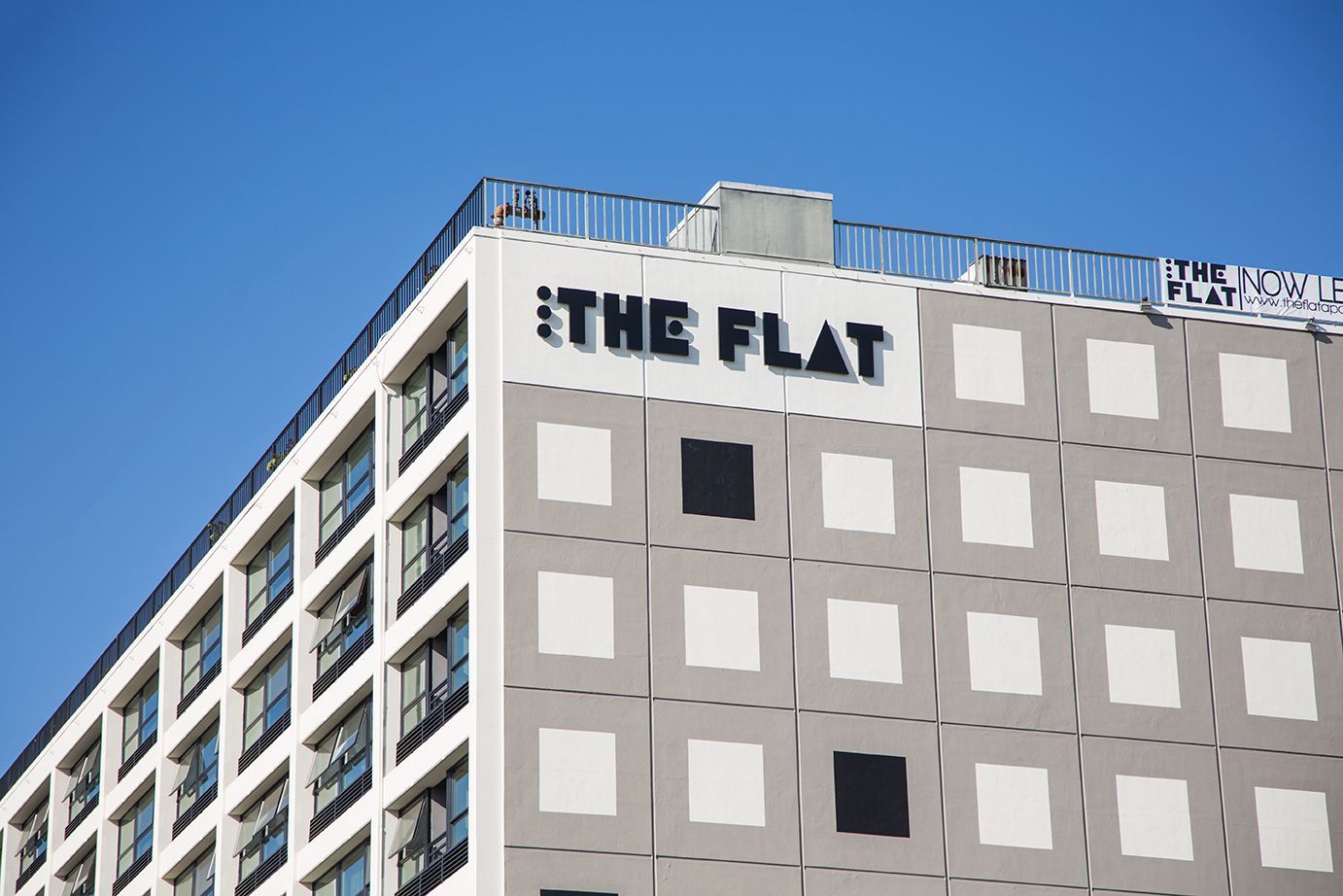 Modern building with “THE FLAT” sign against a clear blue sky