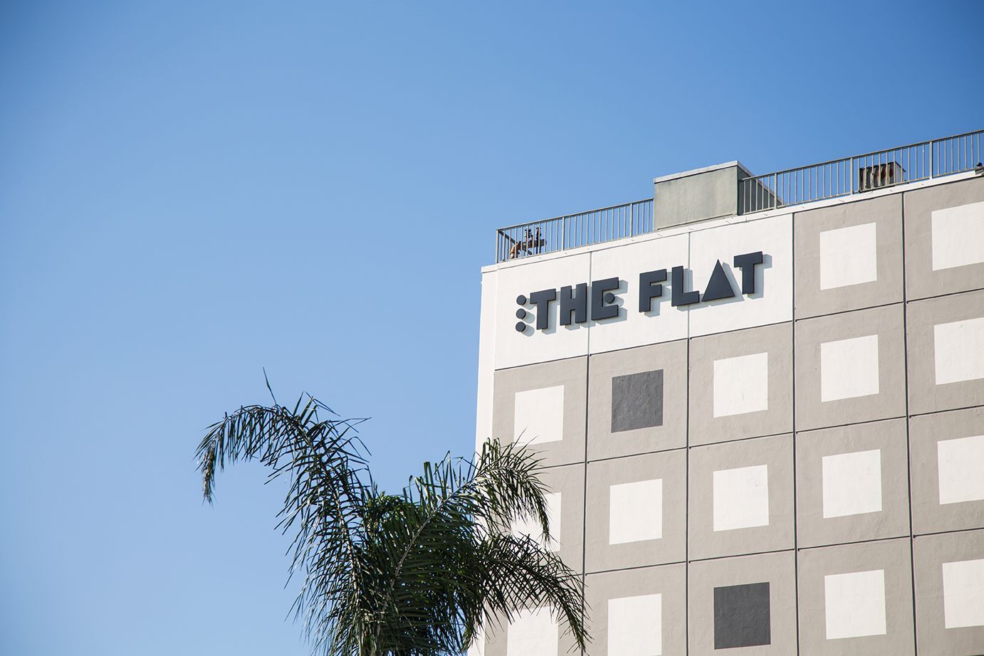 Building exterior with “THE FLAT” sign against a clear blue sky