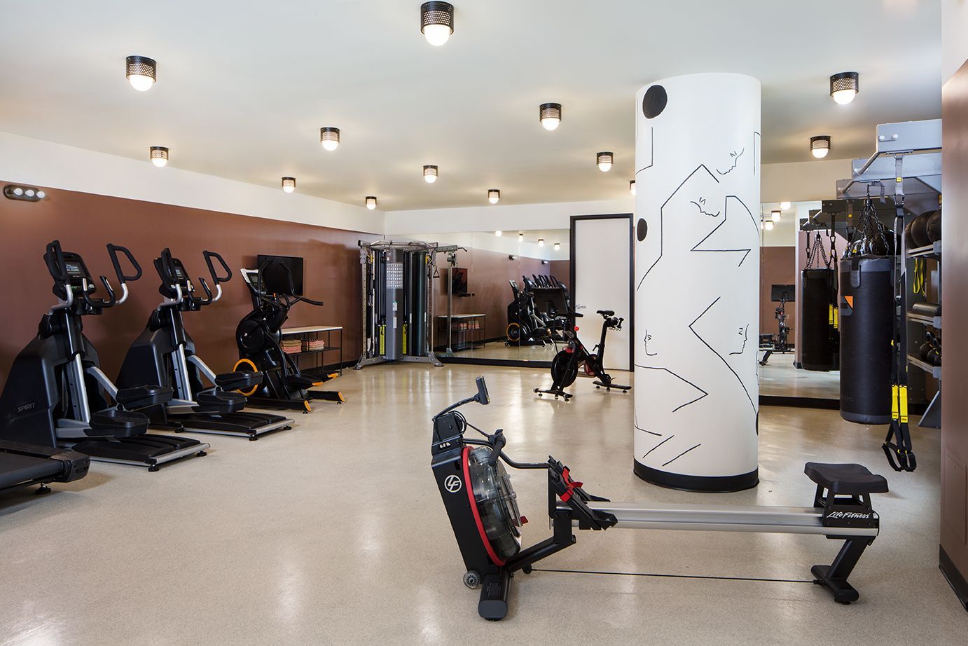 Modern gym interior with cardio machines, weight equipment, and a white pillar in the center