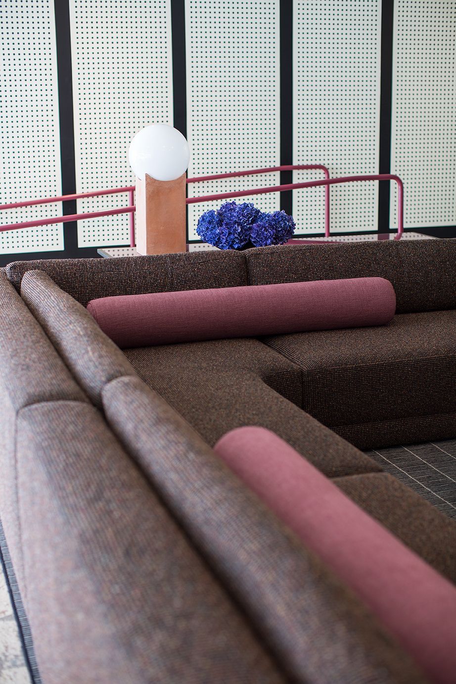 Brown and pink upholstered lounge seating with a red railing and white perforated wall panels in the background