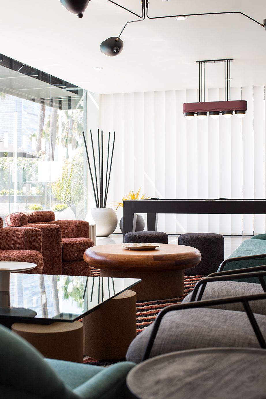 Modern lounge with brown armchairs, round wooden tables, and a hanging light fixture by large windows