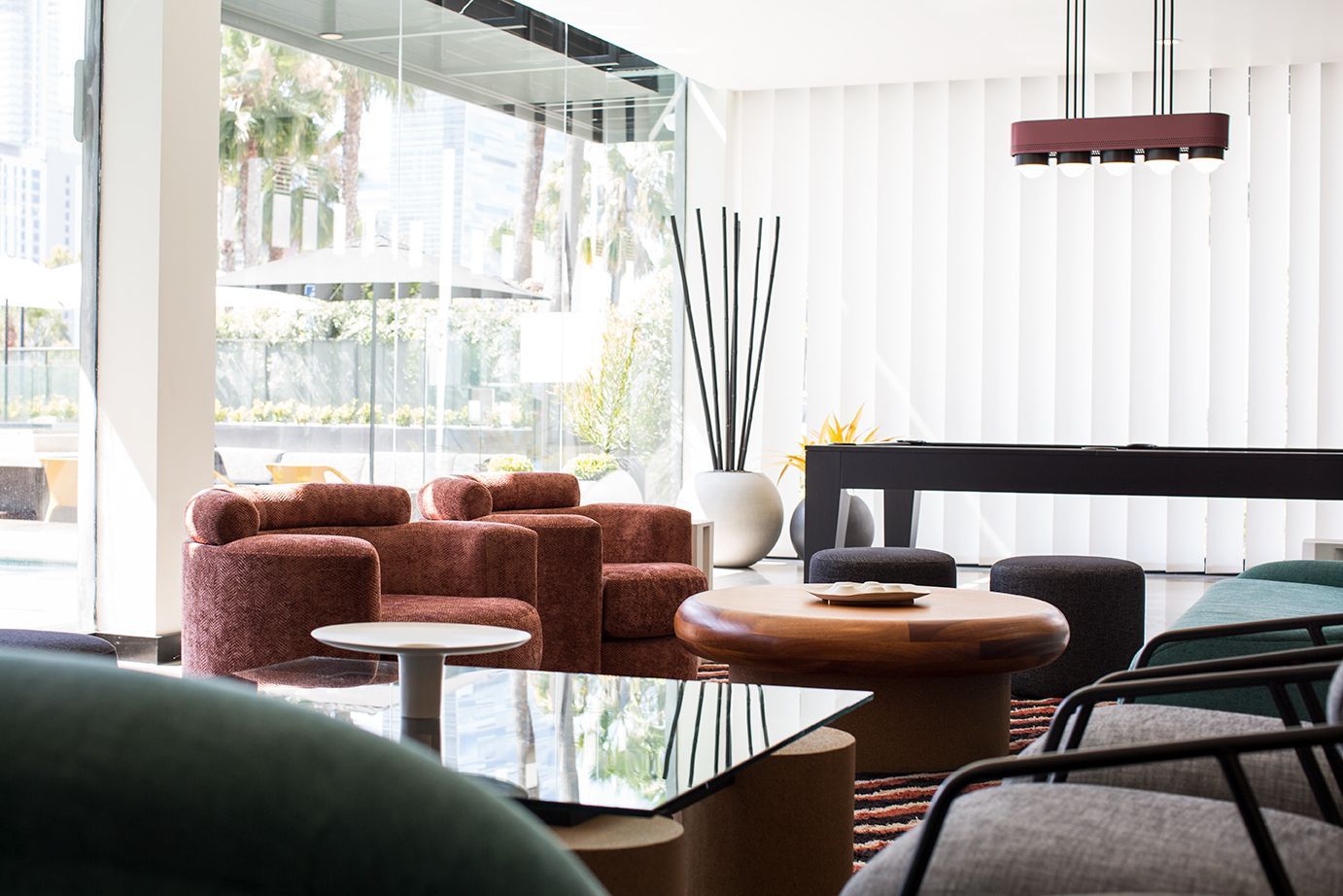 Modern lounge with coral chairs, low tables, and a poolside view through large windows