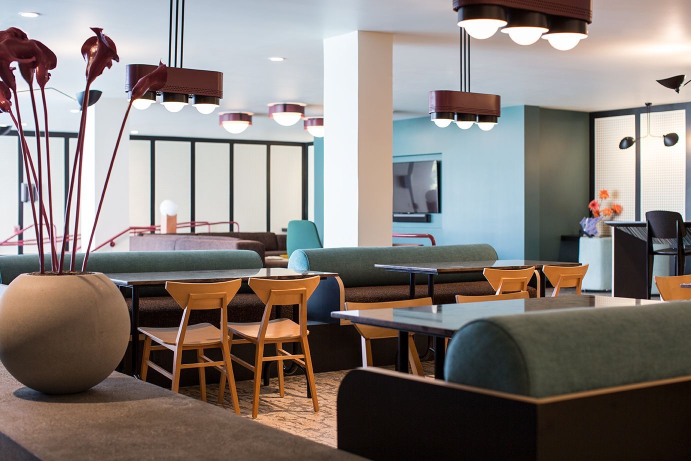 Modern lounge with teal sofas, wooden tables, pendant lights, and a large decorative planter