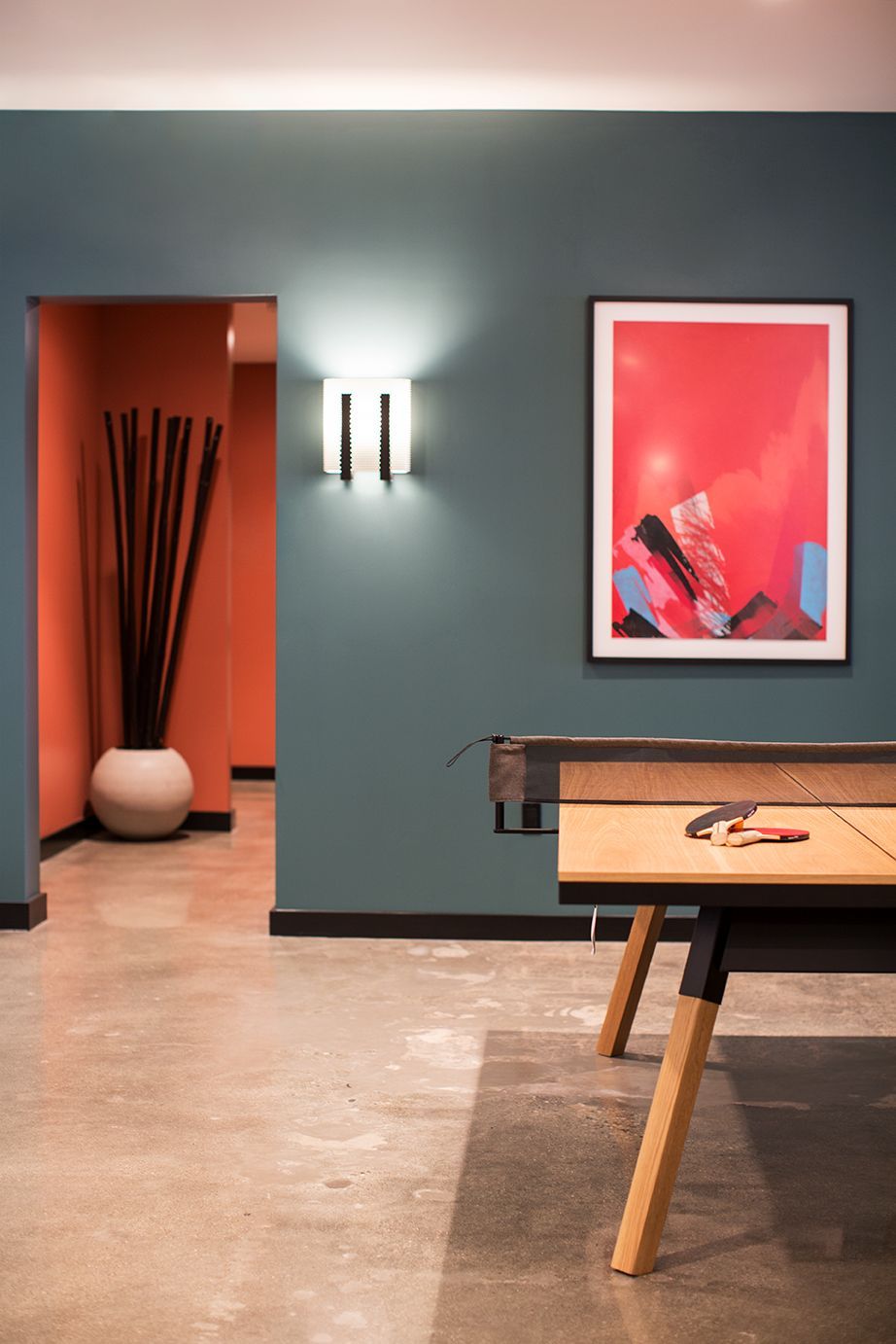 Modern room with teal walls, red doorway, wall art, and a wooden table in the foreground