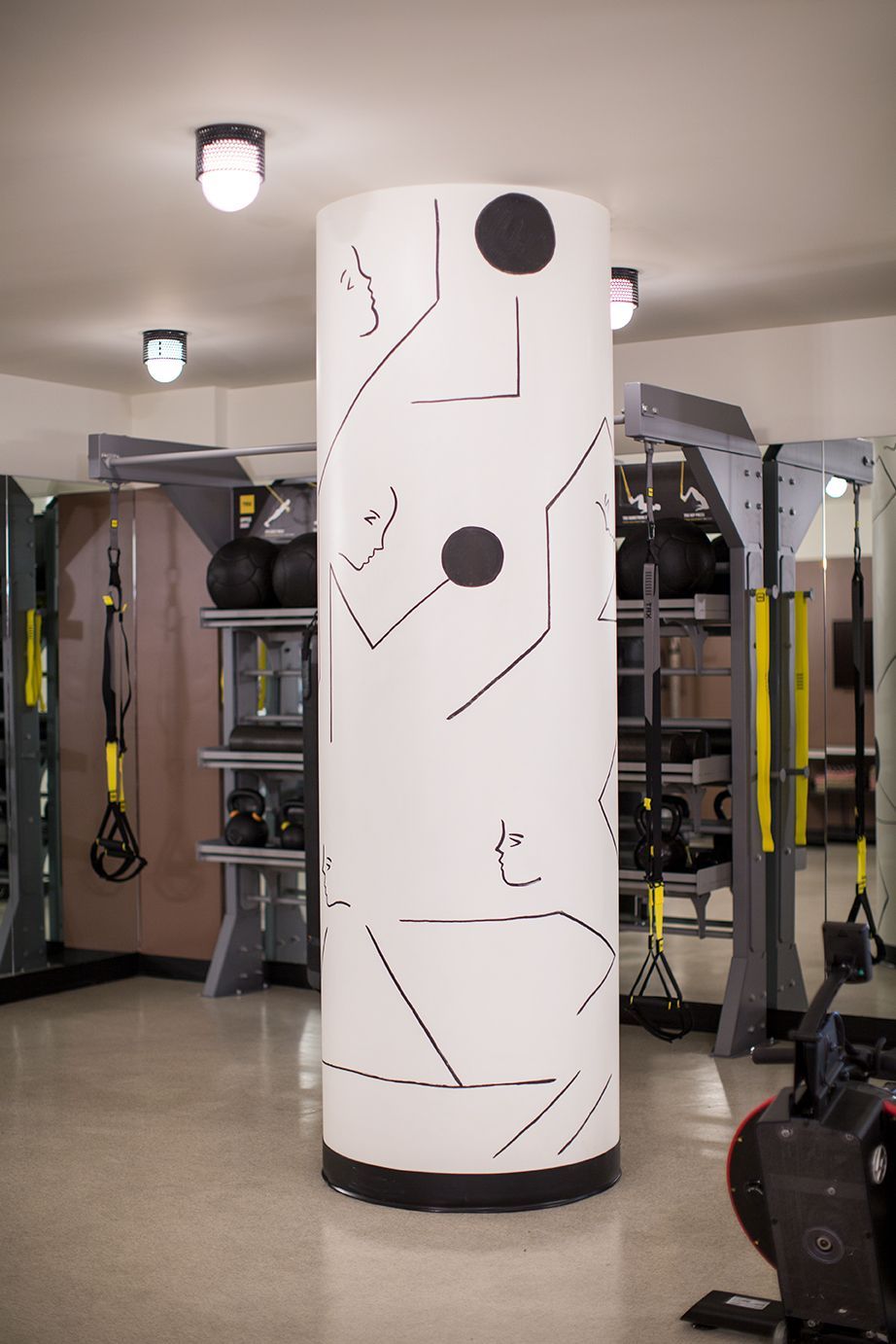 White cylindrical training dummy in a gym, with black target circles and abstract line markings.