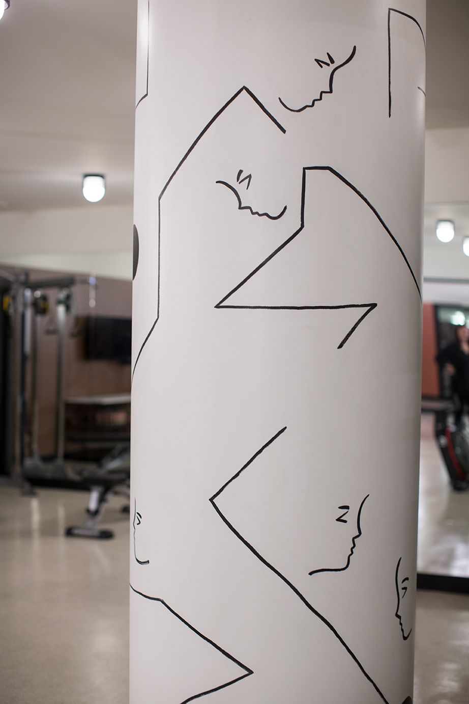 White column with black angular line drawings in a gym-like indoor space.