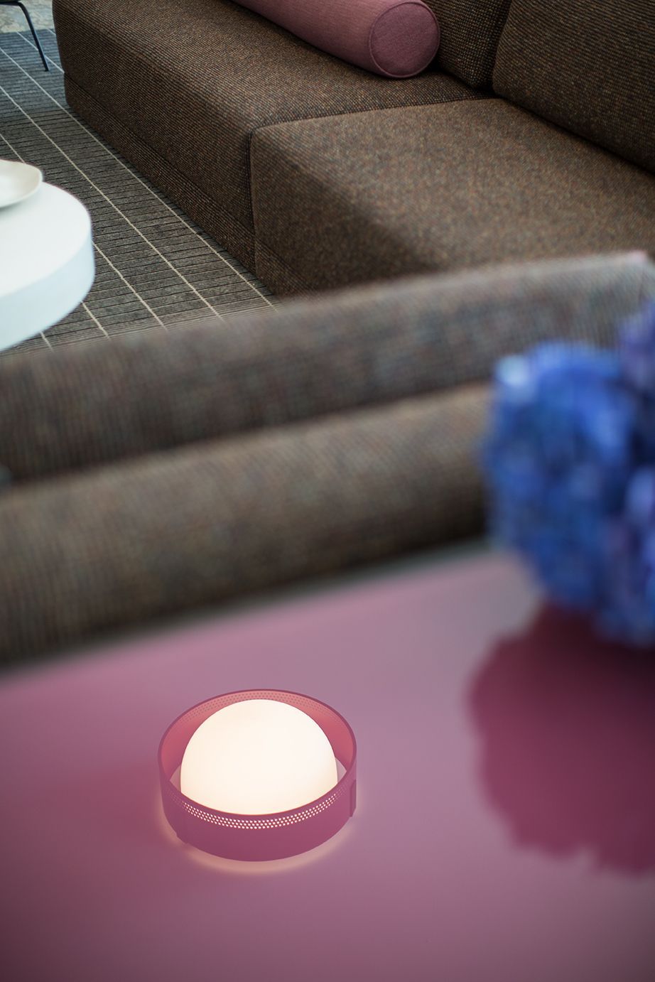 Small lit candle in a pink dish on a table, with a sofa in the background.