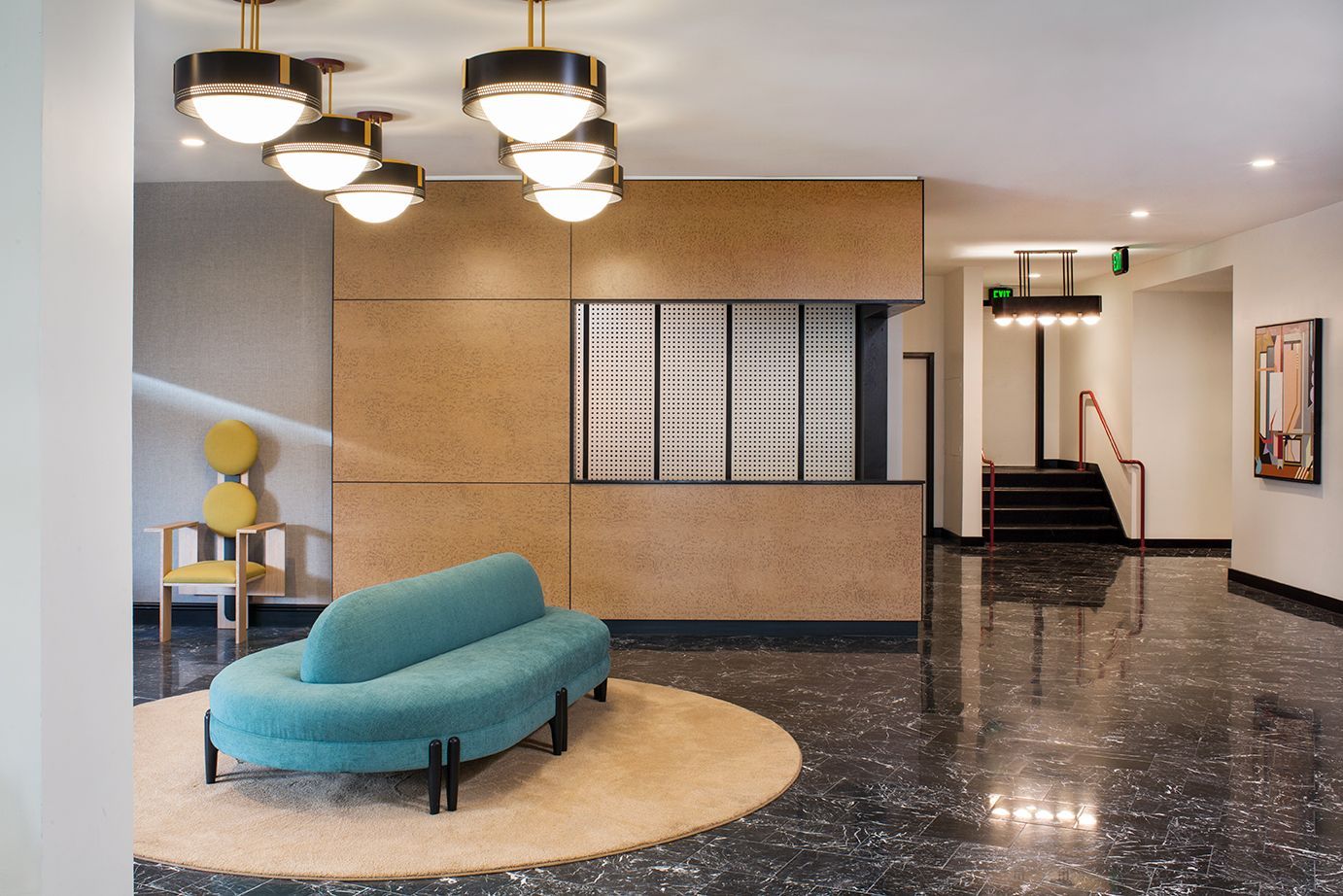 Modern office lobby with teal chaise, round ceiling lights, glossy black floor, and a stairway in back