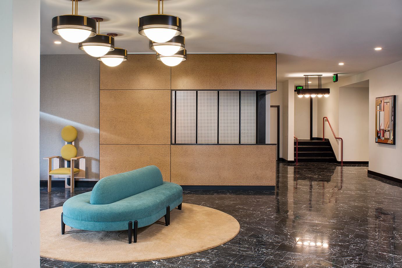 Modern lobby with teal chaise, round rug, hanging lights, reception desk, and glossy black floor