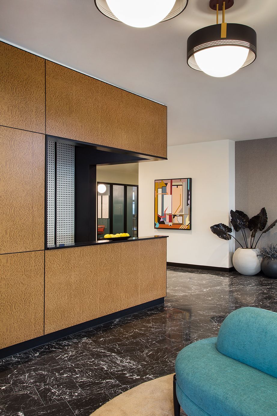 Modern lobby with cork wall, black terrazzo floor, round ceiling lights, and a blue chair.