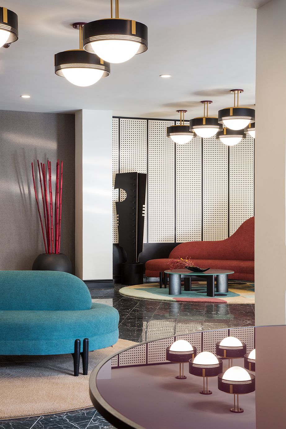 Modern lounge with teal and red seating, patterned screens, and hanging ceiling lights