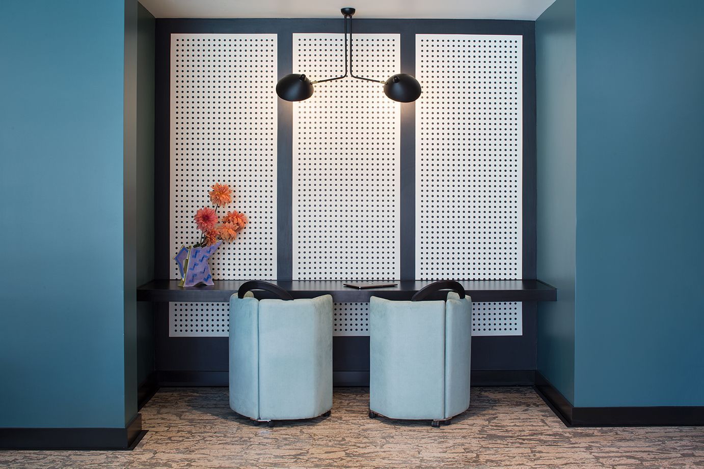 Modern lobby seating nook with two pale chairs, black pendant lights, and a floral arrangement on the left