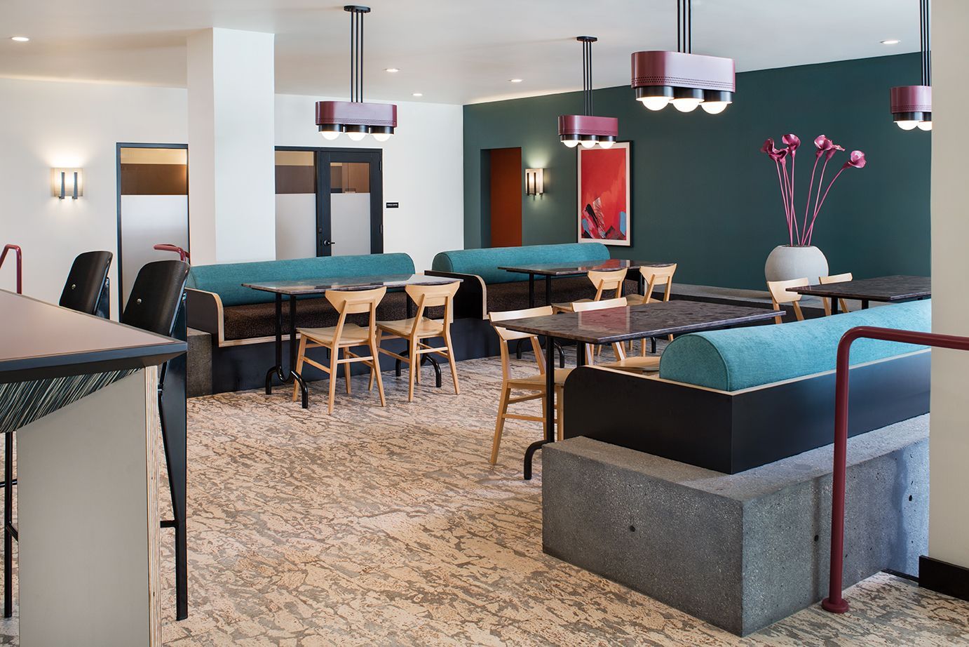 Modern lounge with teal sofas, wooden chairs, pendant lights, and a teal accent wall