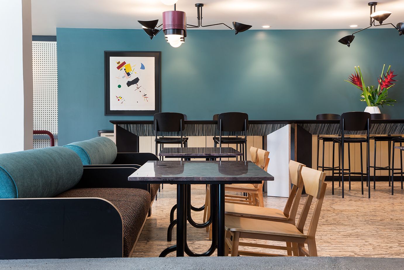 Modern lounge with teal walls, dark booth seating, high tables, and wood chairs under ceiling fans