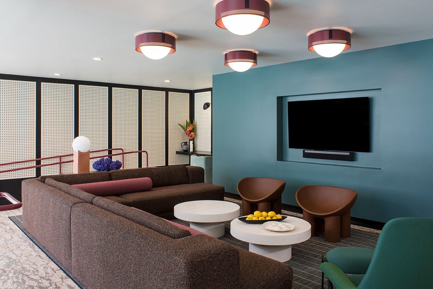 Modern lounge with brown sofas, round tables, wall-mounted TV, and blue accent wall under ceiling lights