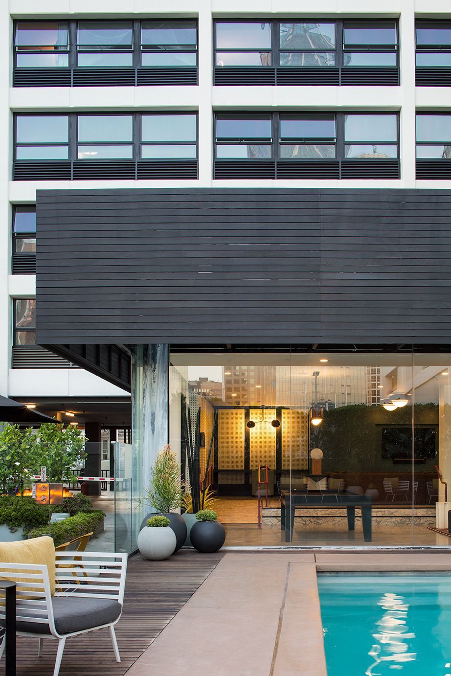 Modern hotel courtyard with a pool, lounge chairs, and a glass entrance under a dark overhang
