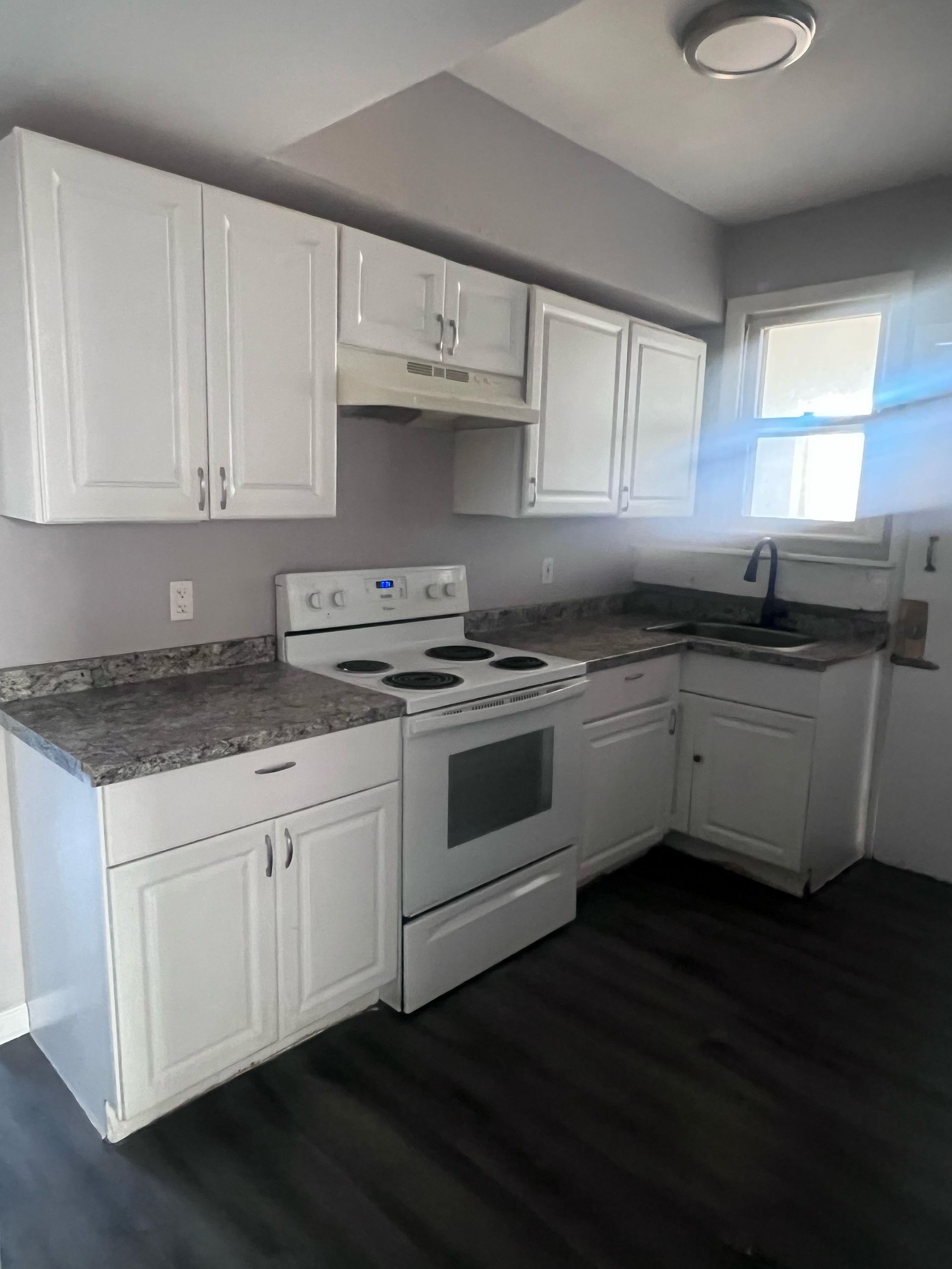 White kitchen with stove, cabinets, granite countertops, and a window over the sink