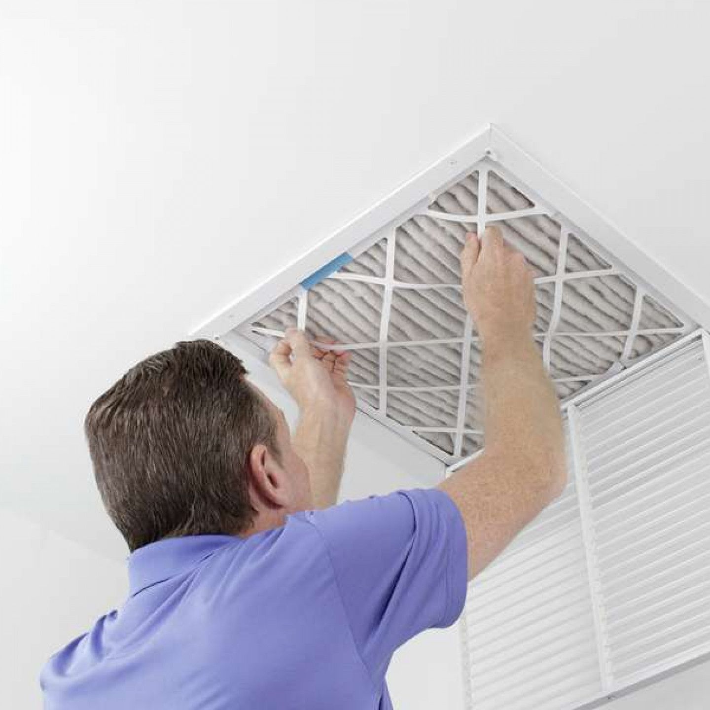 A man in a blue shirt is cleaning an air filter on the ceiling.