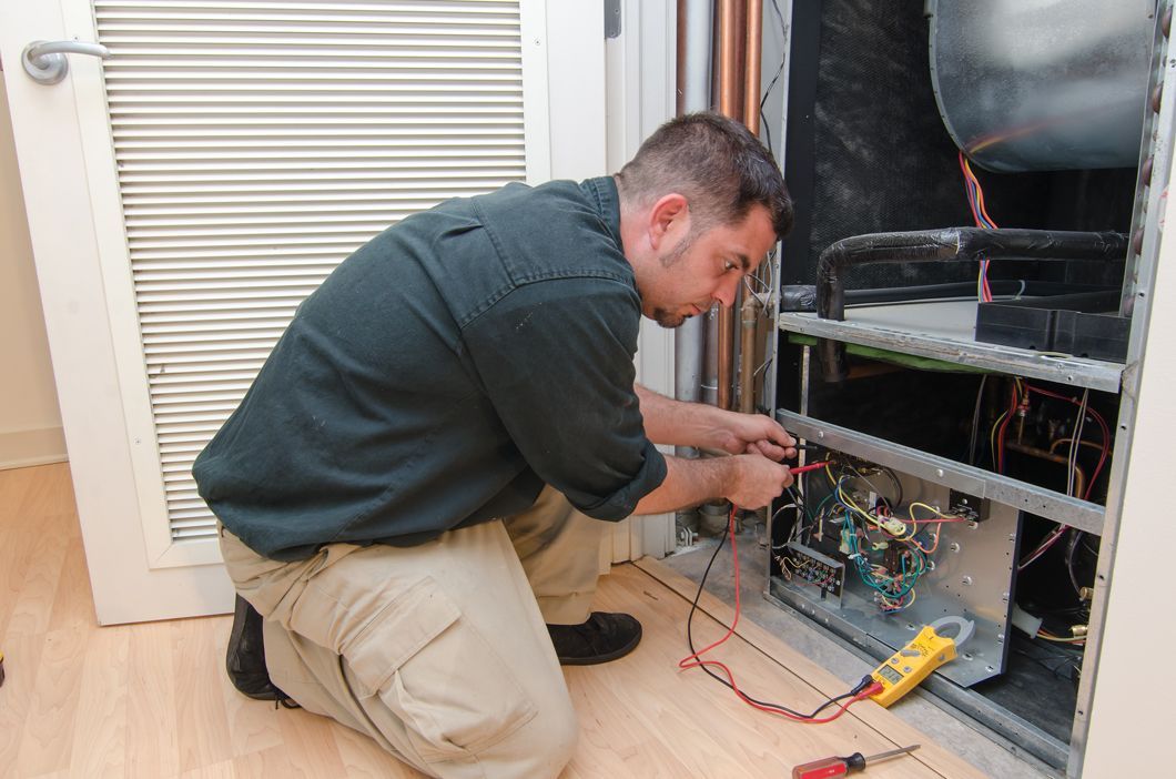 A man is kneeling on the floor working on an air conditioner.