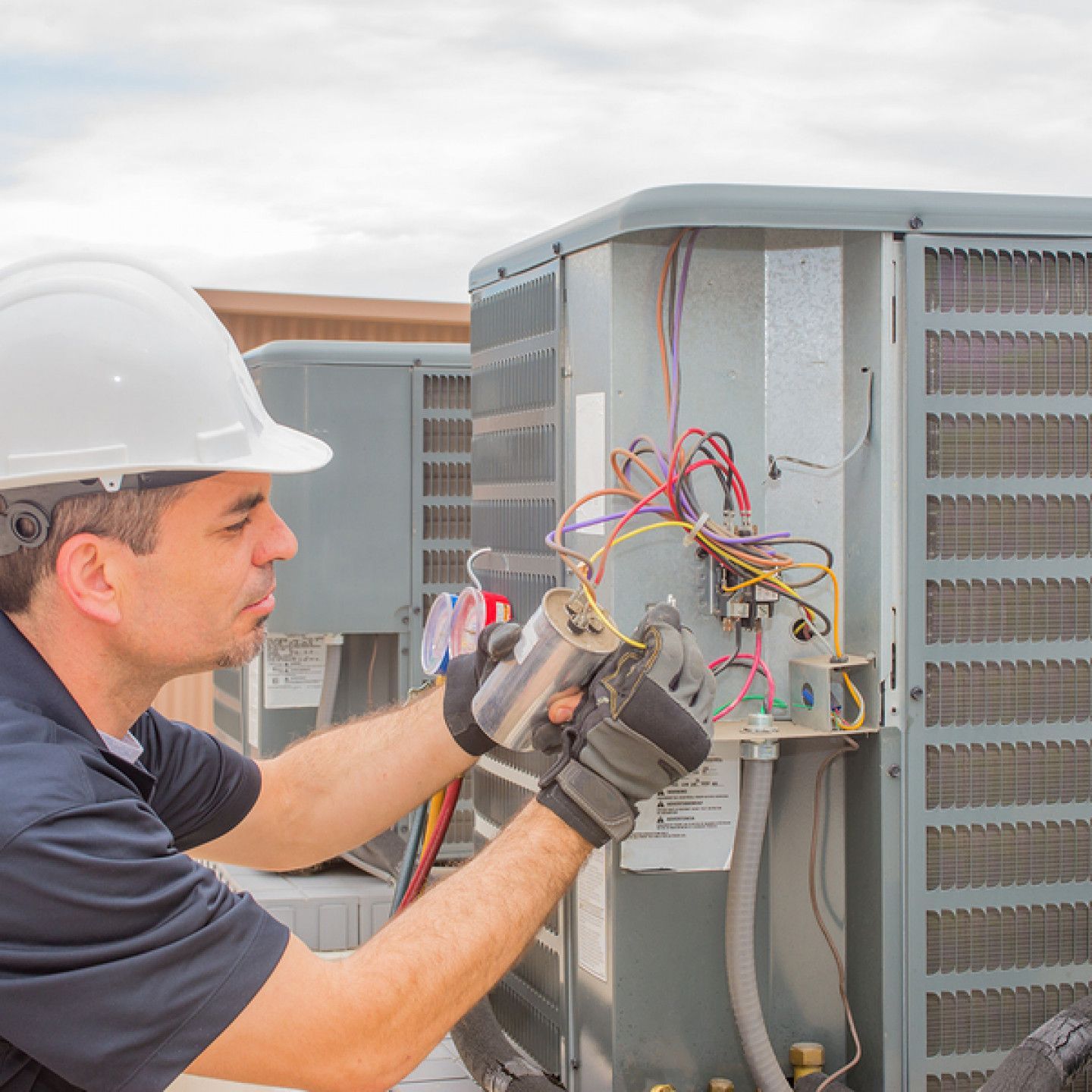 A man wearing a hard hat is working on an air conditioner.