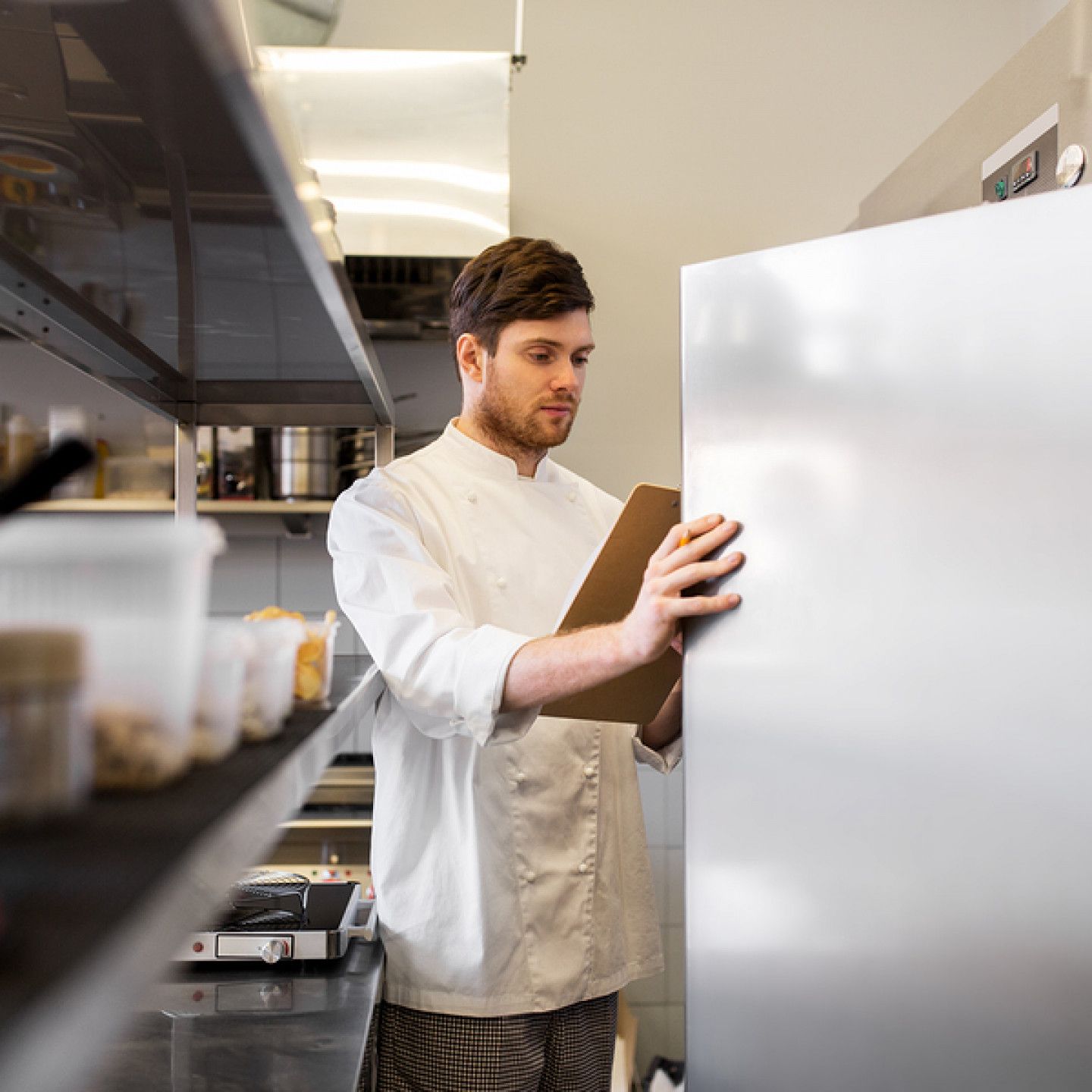 A man is standing in a kitchen looking at a clipboard.